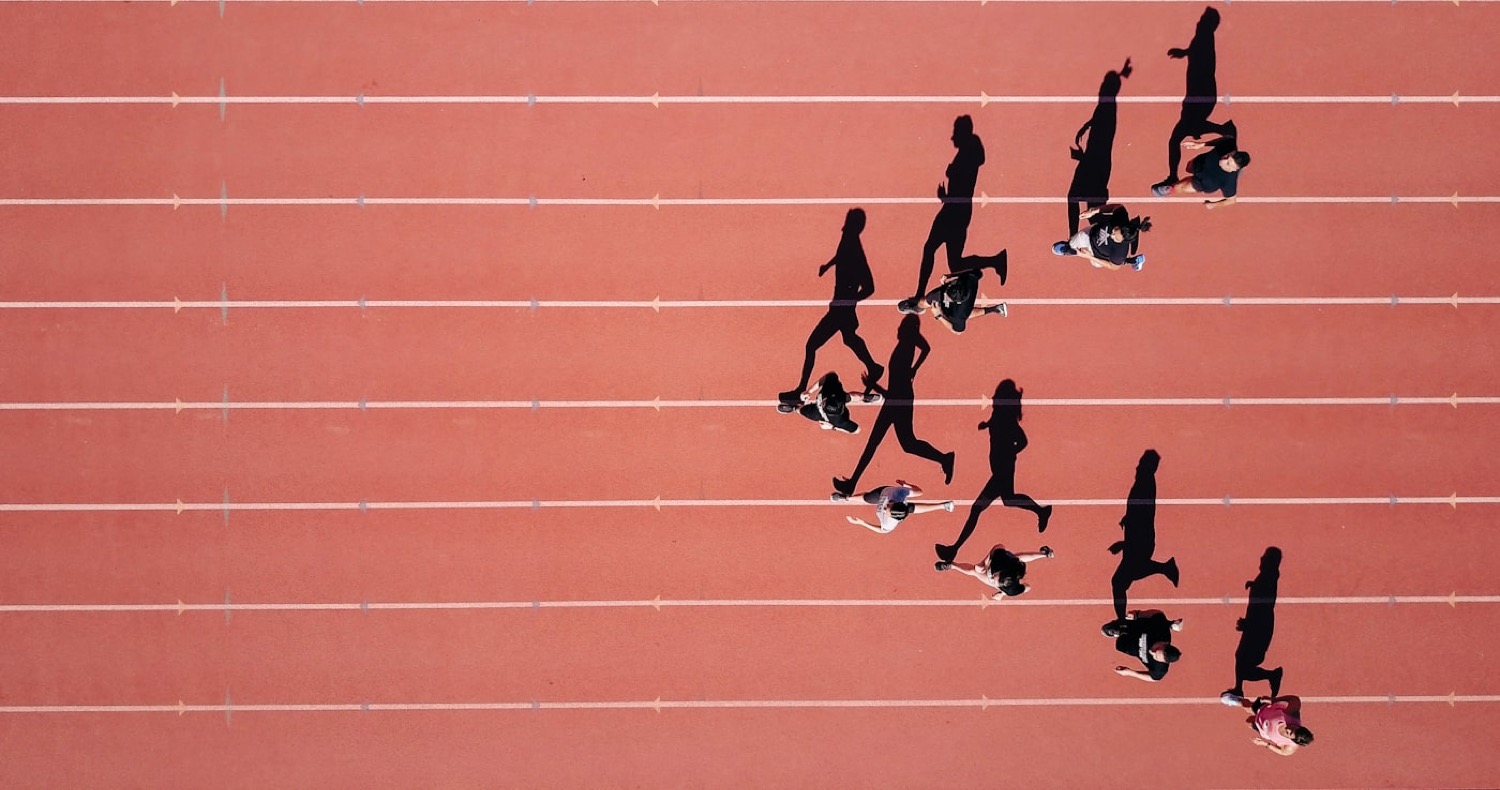 Runners striding across the lanes of a running track, seen from above.